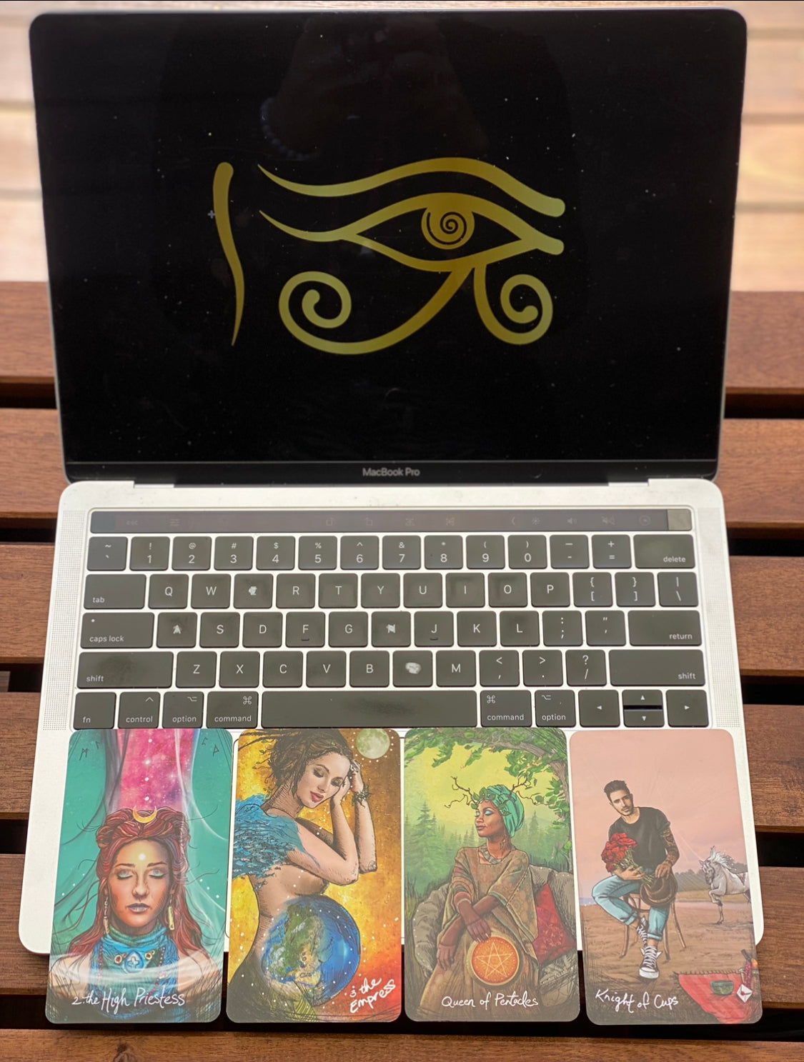 A set of vibrant tarot cards spread out on a laptop, a mac during a spiritual guidance session with the Ra eye part of the Ira Light logo